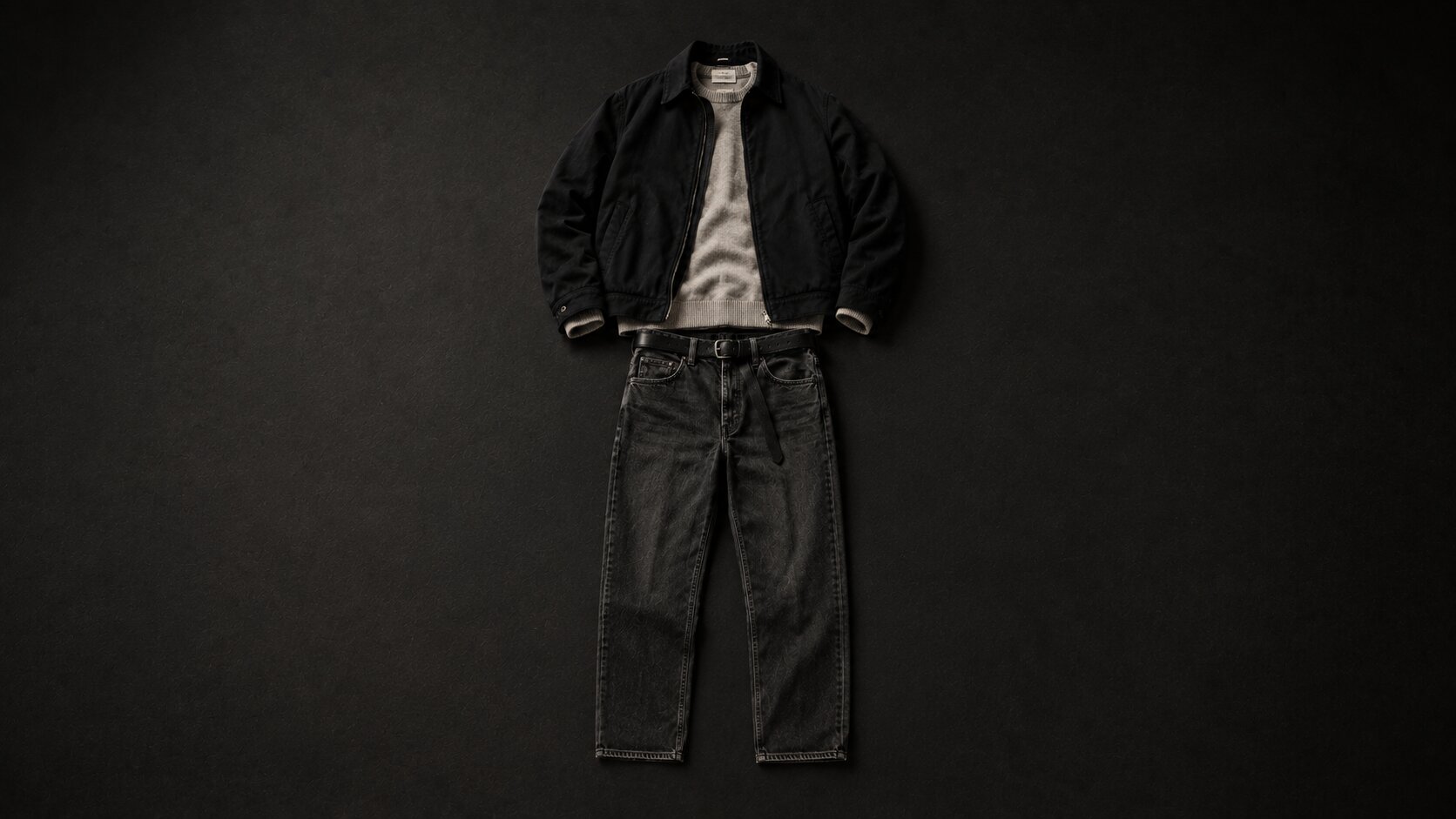 A full outfit laid flat on a dark surface in the order it goes on: jacket, shirt, trousers, belt and one shoe, with the second shoe missing from the row.